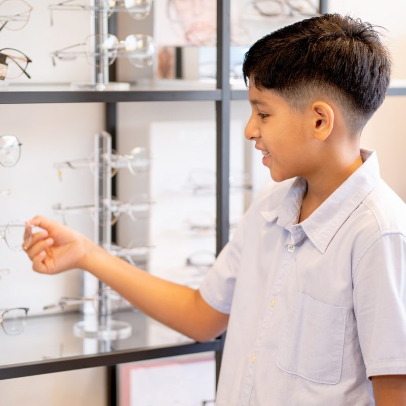 indian-boy-hold-glasses-on-shelf-during-selection-to-buy-some-products-for-his-eyecare.jpg indian-boy-hold-glasses-on-shelf-during-selection-to-buy-some-products-for-his-eyecare.jpg